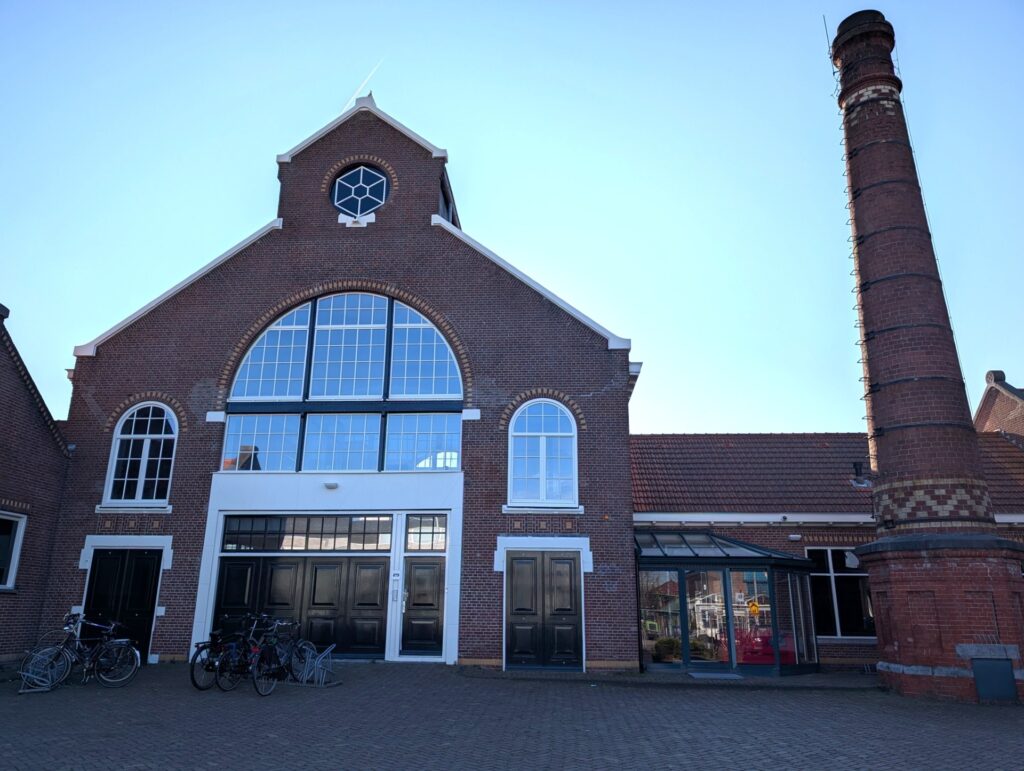 Vooraanzicht van een gerestaureerde bakstenen fabriekshal aan het Gedempt Hamerkanaal met grote ramen en een schoorsteen.